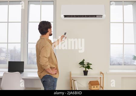 Mann mit Fernbedienung von der Klimaanlage schafft angenehme Temperatur für sich. Stockfoto