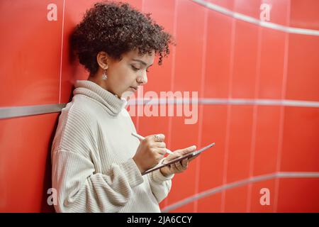 Junge Frau mit einem digitalen Tablet, das in der Nähe der Wand in der U-Bahn steht. Stockfoto