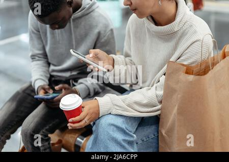 Junge Menschen mit Smartphones und Kaffee zum Mitnehmen sitzen auf einem B Stockfoto