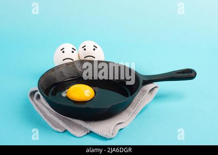 Ein Spiegelei in einer Pfanne, zwei Freunde schauen ihn mit traurigen Gesichtern an, frühstücken am Morgen, komisches Essen, zerbrochene Freundschaft, gesundes Essen Stockfoto