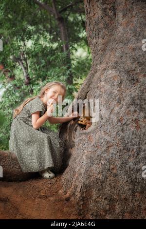 Portrait of adorable Little Kid girl in der Nähe des Baumes mit Eichhörnchen auf sie im Wald Stockfoto