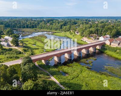 Kuldiga historische rote Backsteinbrücke über den Venta Fluss. 3. längste Backsteinbrücke in Europa. Europas längster Wasserfall im Hintergrund. Kuldiga, Lettland. Stockfoto