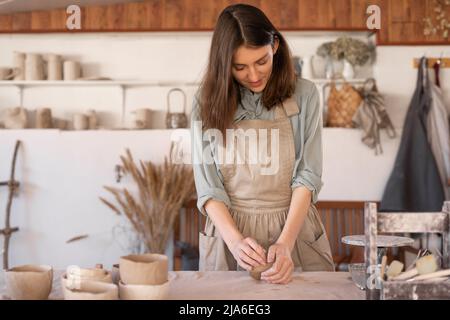 Meister der Kunst Keramik bei der Arbeit glückliche Frau in einer Schürze arbeitet in einer Keramikwerkstatt. In der Werkstatt stellt die Kunsthandwerkerin handgemachte Gerichte her. Stockfoto