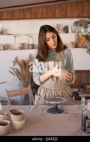 Die junge Kunsthandwerkerin konzentrierte sich während eines Töpferunterrichtete oder Workshops in einem kreativen Studio auf die Bildhauerei einer rohen Tonschale. Frau Keramik Geschäftseigentümer machen Stockfoto