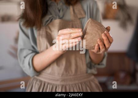 Töpferin bei der Arbeit. Potters Hände aus Ton bilden einen Topf in einem Kreis, Nahaufnahme. Weibliche Schalen aus rohem, nassem Ton Stockfoto