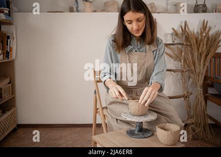 Der kreative Prozess der Nadelarbeit Frau ist in der Formgebung und Handmodellierung von Keramik beschäftigt. Arbeitstisch in der Werkstatt, mit dem der Töpfer arbeitet Stockfoto