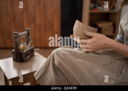 Nahaufnahme von weiblichen Händen, die Töpferarbeiten. Eine Frau formt eine Schale aus weißem Ton, Seitenansicht. Stockfoto