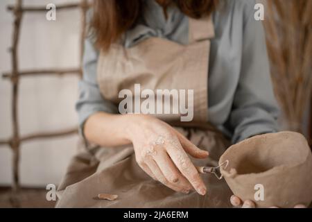 Töpferei und Werkstatt mit Tonkunst-Konzept. Nahaufnahme der Hände einer jungen Keramikerin mit Krug aus ungebackenem Ton. Hände des Handwerkers halten fest Stockfoto