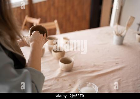 Potter bei der Arbeit. Potters Hände aus Ton bilden einen Topf in einem Kreis. Nahaufnahme von weiblichen Schalen aus rohem, nassem Ton. Stockfoto