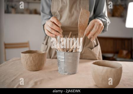 Keramikwerkzeug. Keramische Arbeitswerkzeuge in einer Kunstwerkstatt. Die Hände des Meisters nehmen das Werkzeug. Stockfoto