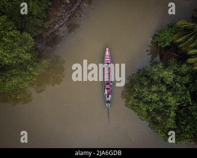 (ANMERKUNG DER REDAKTION: Bild aufgenommen mit Drohne) Luftaufnahme eines Langschwanz-Fischerboots auf einem Kanal entlang des TAPI-Flusses in Surat Thani, Thailand.tägliches Leben in den Mangroven entlang des TAPI-Flusses in Surat Thani, Thailand. Im Laufe des letzten Jahrzehnts haben die Mangroven begonnen, zu verschwinden, da die Garnelenzucht expandiert hat, was zur Entwicklung von Farmen innerhalb der Mangroven führt, die das Ökosystem im Austausch für kurzfristige Gewinne zerstören. Massentourismus nach Thailand und Plastikmüll sind weitere Faktoren, die zum langsamen Verschwinden der Mangroven beitragen. Stockfoto