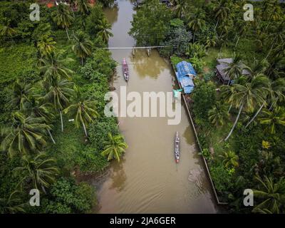 (ANMERKUNG DER REDAKTION: Bild aufgenommen mit Drohne) eine Luftaufnahme von Langschwanz-Fischerbooten auf einem Kanal entlang des TAPI-Flusses in Surat Thani. Thailand.Alltag in den Mangroven am TAPI-Fluss in Surat Thani, Thailand. Im Laufe des letzten Jahrzehnts haben die Mangroven begonnen, zu verschwinden, da die Garnelenzucht expandiert hat, was zur Entwicklung von Farmen innerhalb der Mangroven führt, die das Ökosystem im Austausch für kurzfristige Gewinne zerstören. Der Massentourismus nach Thailand und Plastikmüll gehören zu den anderen Faktoren, die zum langsamen Verschwinden der Mangrove beitragen. Stockfoto