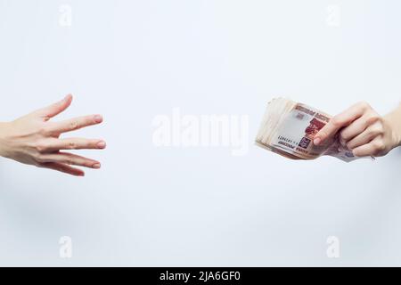 Die Palme greift nach einer Packung von fünftausendsten Scheinen, die in der anderen Hand auf weißem Hintergrund eingequetscht sind Stockfoto