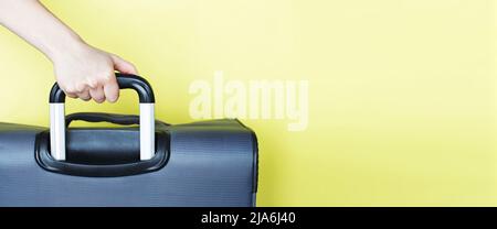 Hand hält einen Koffer isoliert auf einem gelben Hintergrund. Passagiere, die am Wochenende ins Ausland reisen. Konzept der Flugreise. Space Mock Up kopieren. banne Stockfoto