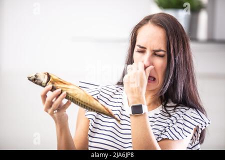 Frau hält stinkenden Fisch hält ihre Nase mit angewiderten Gesichtsausdruck aus dem Geruch. Stockfoto