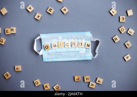 Word omicron aus Holzblöcken mit medizinischer Maske auf grauem Hintergrund Stockfoto