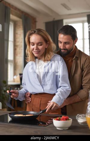 Porträt eines schönen jungen multiethnischen Paares, das morgens in der Küche das Frühstück zusammen kocht Stockfoto