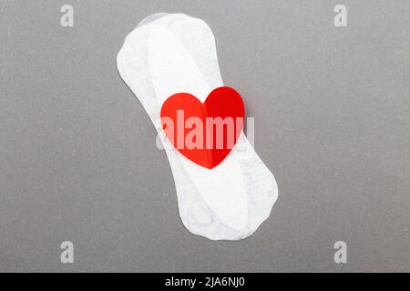 Feminine Damenunterlage mit rotem Herz auf grauem Hintergrund. Stockfoto