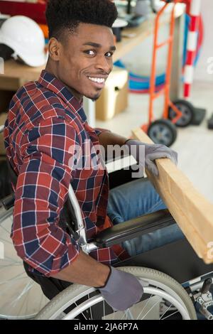 Junger Mann im Rollstuhl versucht sich selbst, sein Bücherregal zu falten Stockfoto