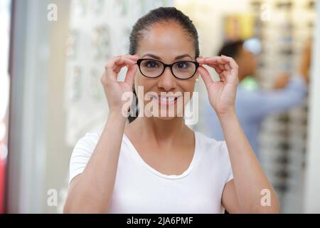 Frau, die im Optikerladen eine Brille probiert Stockfoto