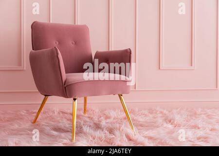 Ein eleganter Sessel mit pinkfarbenem Samt, der auf einem flauschigen Teppich steht. Moderne, luxuriöse Innenausstattung. Stockfoto