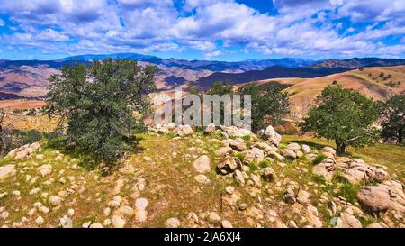 Detail der Bergspitze mit Frühlingsbäumen und Felsbrocken mit Blick auf endlose Bergketten Stockfoto