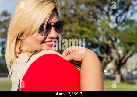 Portrait schöne blonde plus size lateinamerikanische argentinische junge Frau mit Sonnenbrille lächeln im Freien Blick auf die Kamera, an einem sonnigen Tag im Park w Stockfoto