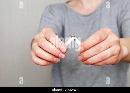 Eine junge Frau, die eine zerbrochene Zigarette in den Händen hält Stockfoto