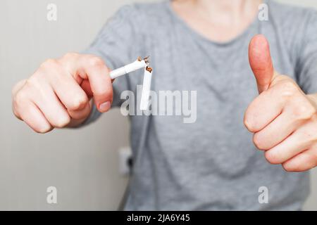 Eine junge Frau, die eine zerbrochene Zigarette in den Händen hält Stockfoto
