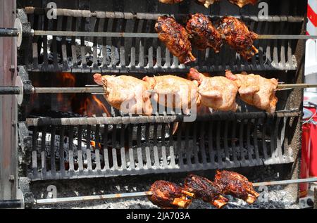 Industrielle Rotisserie mit Spieß-gebratenen Hühnern und Schweinshank und Schinkenfleisch beim Kochen im Restaurant des Dorffest Stockfoto