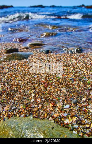 Strand mit Wellen und gefüllt mit glatten Stücken aus buntem Glas Stockfoto