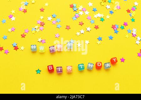 Inschrift Happy Birthday und bunte Konfetti in Form von Sternen auf einem gelben Hintergrund Stockfoto