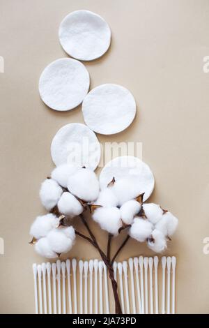 Flauschige Baumwollblumen-Wattestäbchen und Wattestäbchen auf beigem Hintergrund mit Platz zum Kopieren. Hygienisches Einwegprodukt Stockfoto