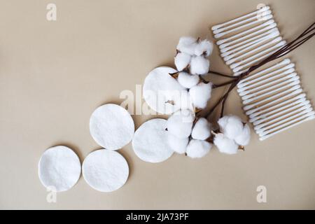 Flauschige Baumwollblumen-Wattestäbchen und Wattestäbchen auf beigem Hintergrund mit Platz zum Kopieren. Hygienisches Einwegprodukt Stockfoto