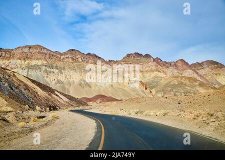 Schwarze asphaltierte Straße im Death Valley, die sich durch die Wüste schlängelt Stockfoto