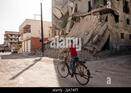 Darayya, Syrien - April, 2022: Kind auf dem Fahrrad auf der Straße in der zerstörten Stadt nach dem syrischen Bürgerkrieg. Stockfoto