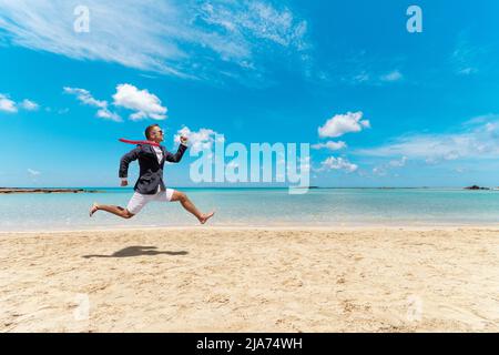 Ein lustiger Geschäftsmann läuft von der Büroarbeit am Strand. Sommerferienkonzept. Stockfoto