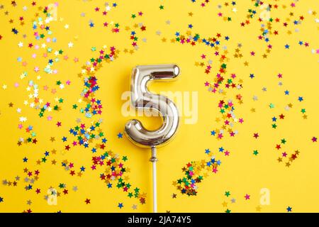 Fünf Jahre Geburtstagsfeier. Nummer fünf mit einem bunten Konfetti in Form von Sternen auf gelbem Hintergrund Stockfoto