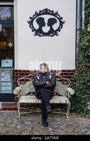 Älterer Mann, der auf einer dekorativen Metallbank vor dem Friseurladen in der Oderberget Straße, Prenzlauer Berg, Berlin, sitzt. Stockfoto