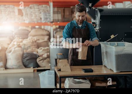 Uniformierte Arbeiter verpackt geröstete Kaffeebohnen in Verpackungen zum Verkauf Stockfoto
