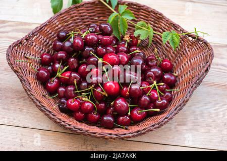 Frische rote Süßkirschen, in einem Weidenkorb auf Holzboden Stockfoto