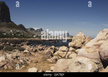 Panoramablick auf die Häuser in der Siedlung Rooi-Els zwischen hohen Bergklippen und der felsigen, zerklüfteten Küste Südafrikas. Stockfoto