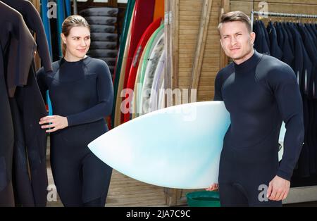 Junges Paar, das im Beach Club surfen will, wählt Boards und Surfanzüge Stockfoto