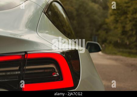 Weißes Elektroauto Tesla Model 3 Hinteres Bremslicht an einer deutschen Forststraße Stockfoto