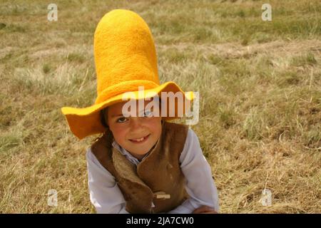 Mädchen in einem hohen gelben Bauernhut mit dem breiten Rand läuft im Sommer auf dem grünen Feld. Sie hat ein langes braunes Haar, ein einziges Zopf hängt herunter Stockfoto