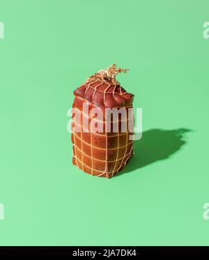 Ein großes Stück geräucherter Käse, mit einer Schnur umwickelt, isoliert auf einem grünen Hintergrund. Ein einzelner Chunk geräucherter Käse in hellem Licht auf einem bunten Tabl Stockfoto