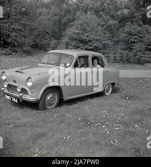 1950s, historisches Großbritannien nach dem Krieg, und parkte auf einem Feld in einem Park, ein Mann und zwei Damen saßen in einem Wagen der Ära Austin A40 in Cambridge. Der Herr raucht eine Pfeife, während die beiden Damen auf der Rückseite des 4-türigen kleinen Familienwagens sitzen. In dieser Zeit war es eine beliebte Freizeitbeschäftigung, einen Tag lang an einer malerischen Stelle zu fahren und gilt als das goldene Zeitalter des Autofahrens. Der vom britischen Hersteller Austin Motor Company hergestellte Austin Cambridge wurde von 1954 bis 1971 in verschiedenen Versionen und Karosserieformen produziert. Stockfoto