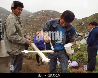 Junge Männer malen das Kreuz ihrer verstorbenen Verwandten auf dem Friedhof von La Esperanza im Bezirk Villa el Salvador in Lima. Es ist eines der größten in Amerika und empfängt fast zwei Millionen Besucher pro Jahr, nur am Tag der Toten. Stockfoto