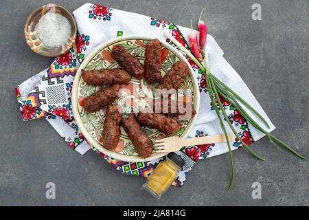 Rumänische, traditionelle Fleischbrötchen, genannt „mici“ oder „mititei“ Auf einer Keramikplatte gegrilltes Hackfleisch Stockfoto