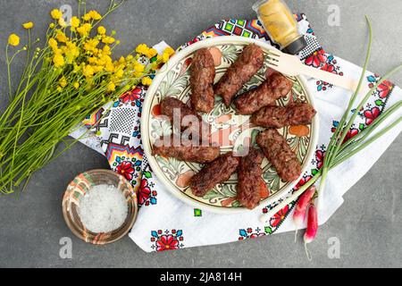 Traditionelle Fleischbrötchen, auf einem Keramikplatte „mititei“ genannt, mit einem Bouquet von Butterblumen Stockfoto